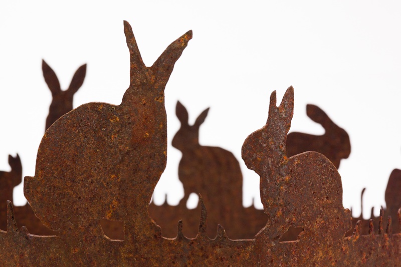 Silhouettes of several Easter bunnies cut out of rusted metal for Easter I words