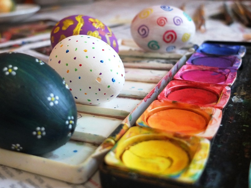 Four Easter eggs, one with a small chip, in the process of being painted next to artist paint palette for P Easter phrase painted eggs